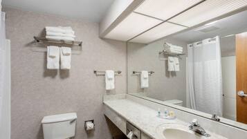 A bathroom with a toilet, sink, and mirror. There are towels on a rack and a shower curtain.