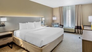 Une chambre d’hôtel avec un grand lit, des tables de chevet, un bureau, une chaise, une fenêtre avec des rideaux et un appareil de climatisation.
