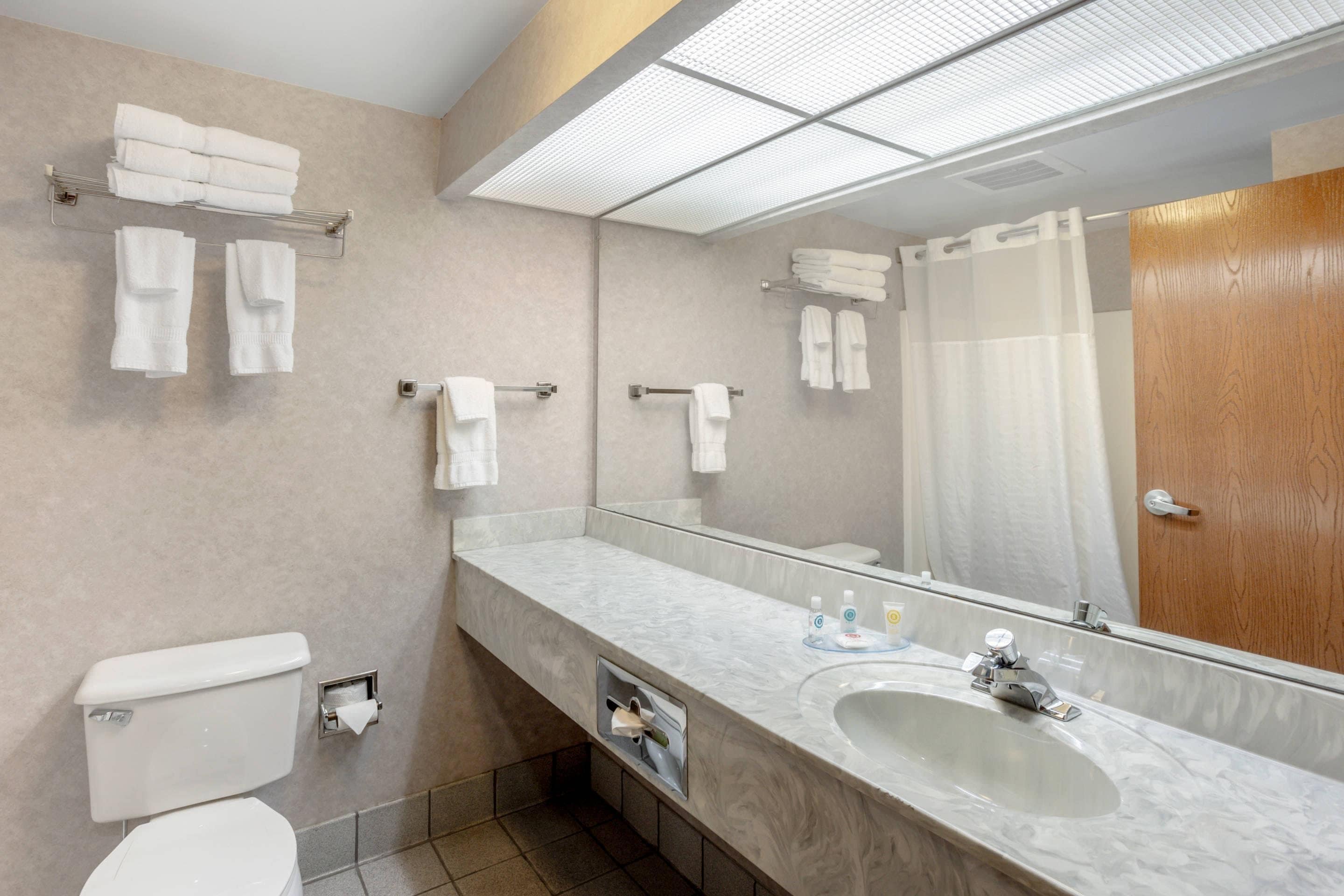 A modern bathroom with a marble sink, a toilet, a shower with a glass door, and multiple towel racks.