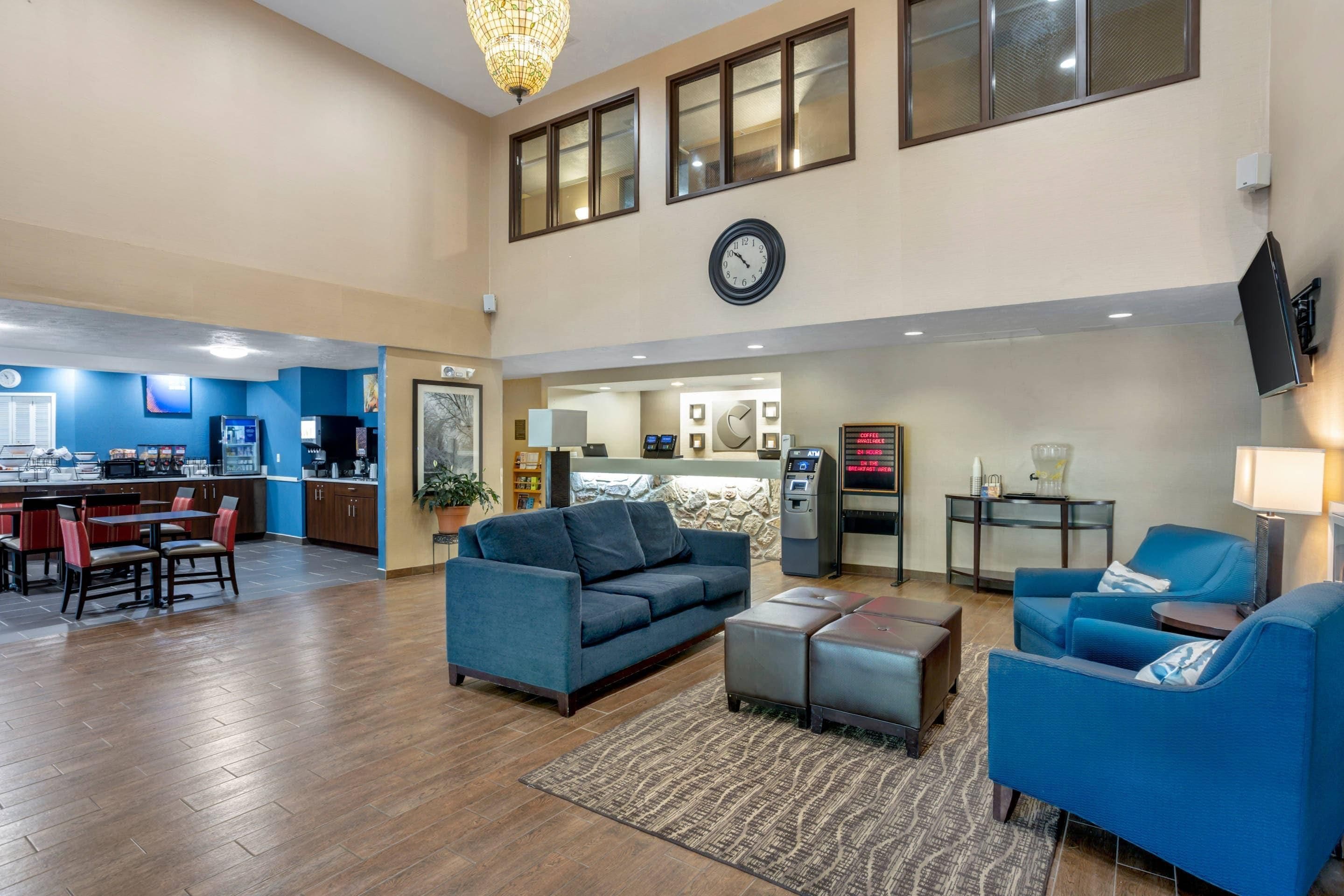 A hotel lobby with a dining area, seating, a clock, and an ATM.