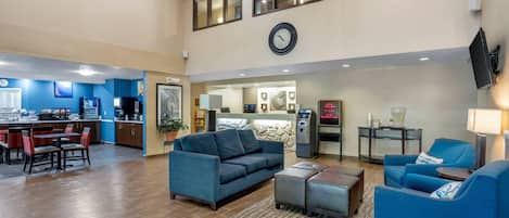 A hotel lobby with a dining area, seating, a clock, and an ATM.