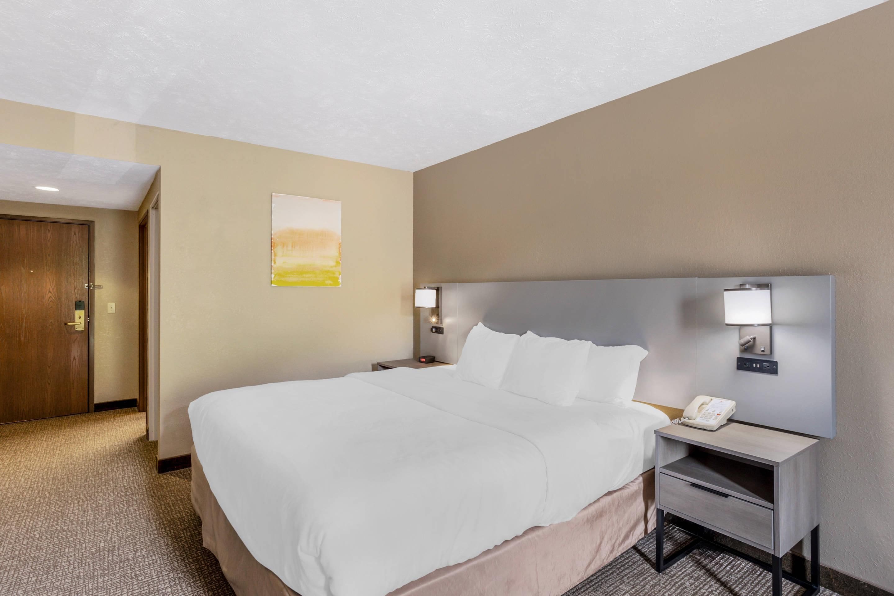 A hotel room with a large bed, bedside tables, a phone, and a painting on the wall.