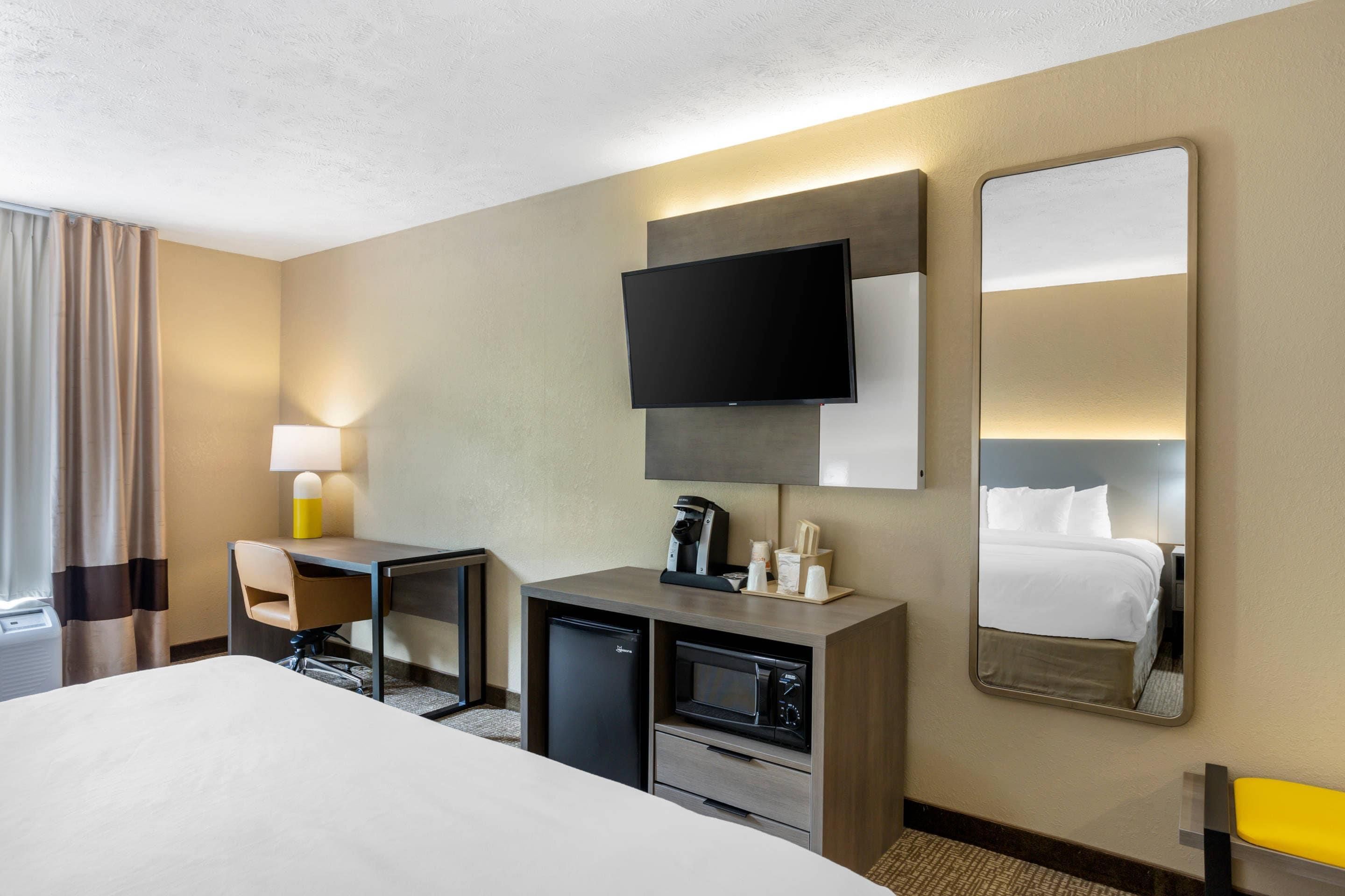 A hotel room with a bed, a desk with a chair, a television, a coffee machine, and a microwave.