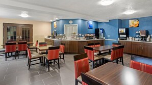 Une salle à manger d’hôtel avec plusieurs tables et chaises, un comptoir de cuisine et une horloge au mur.