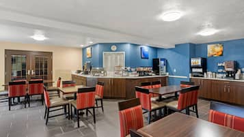 A hotel dining area with multiple tables and chairs, a kitchen counter, and a clock on the wall.