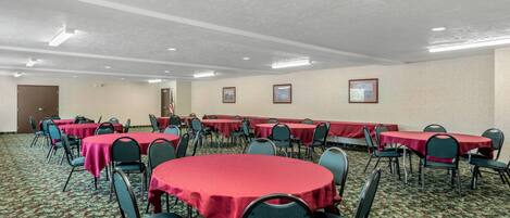 A conference room with multiple tables and chairs, carpeted floor, and framed pictures on the walls.