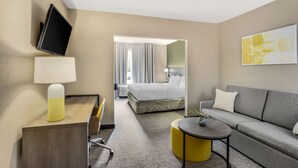 Een hotelkamer met een bed, een bank, een bureau met lamp, een televisie en een schilderij aan de muur.