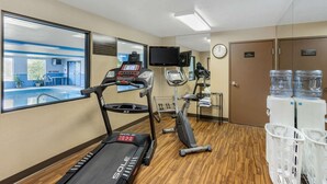 Een fitnessruimte met loopbanden, een crosstrainer, een hometrainer, een waterkoeler en uitzicht op een zwembad.