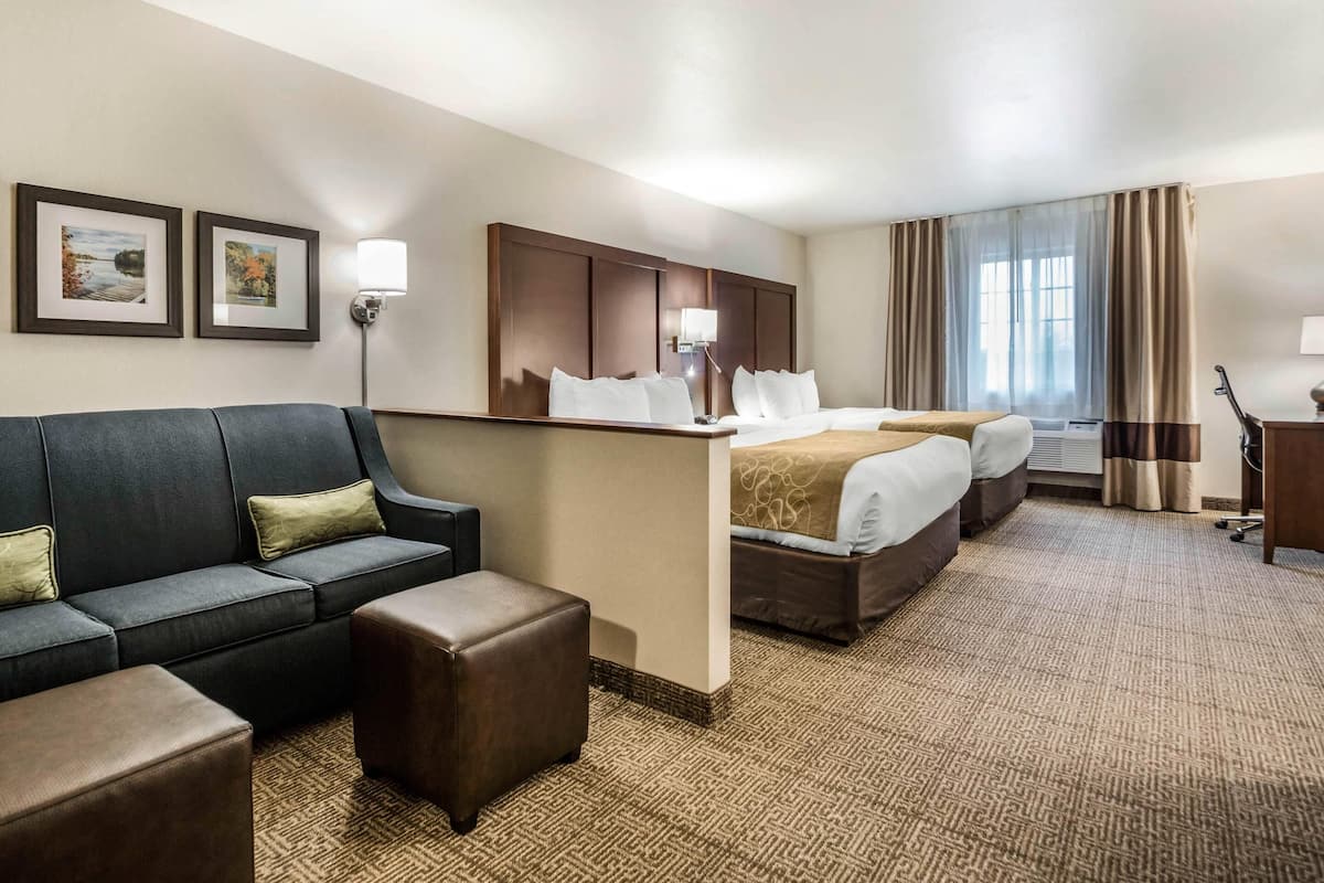 A hotel room with a sofa, two beds, a desk, and a lamp.