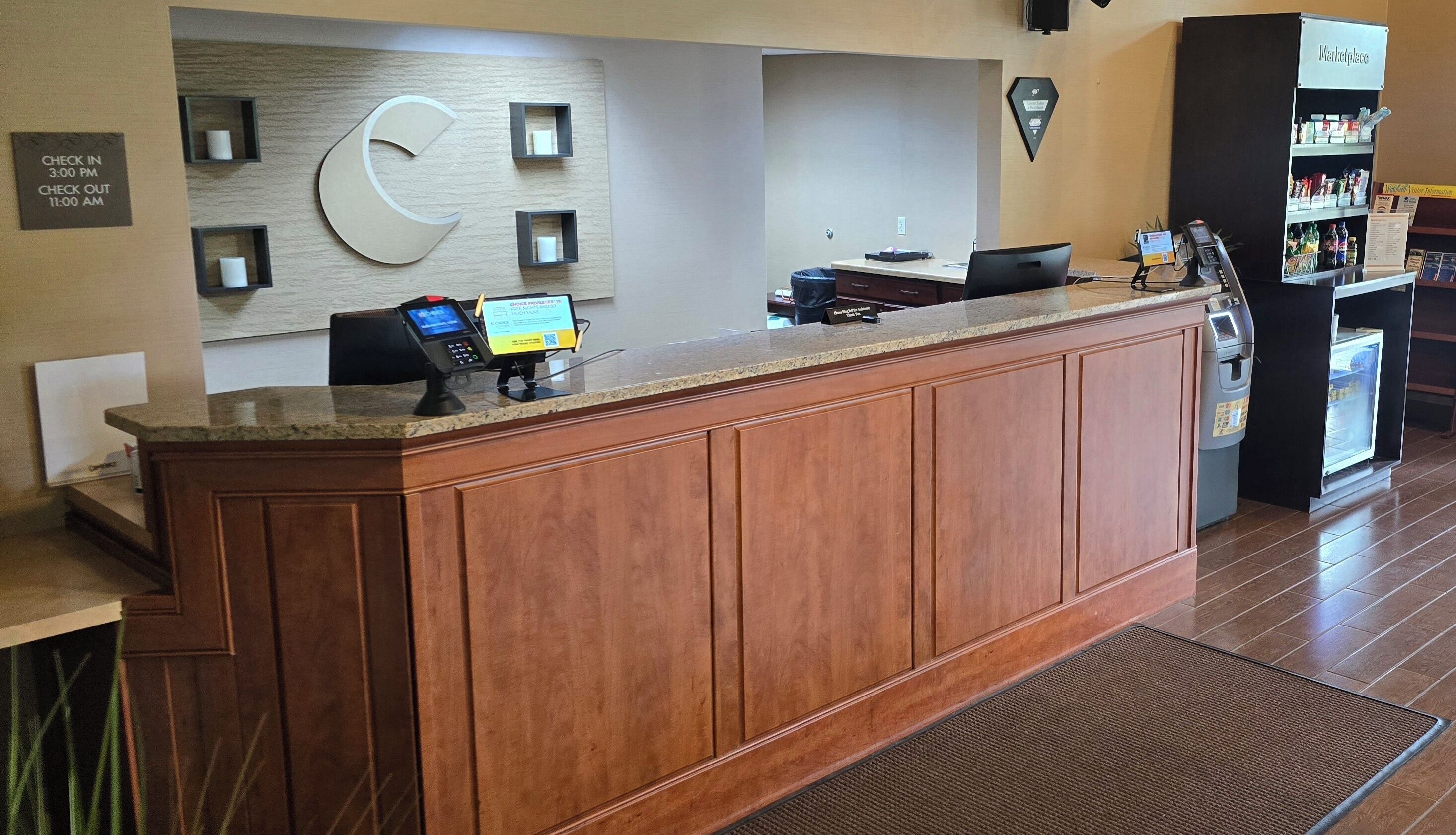 A reception desk with a digital kiosk, a clock, and a self-service beverage machine.