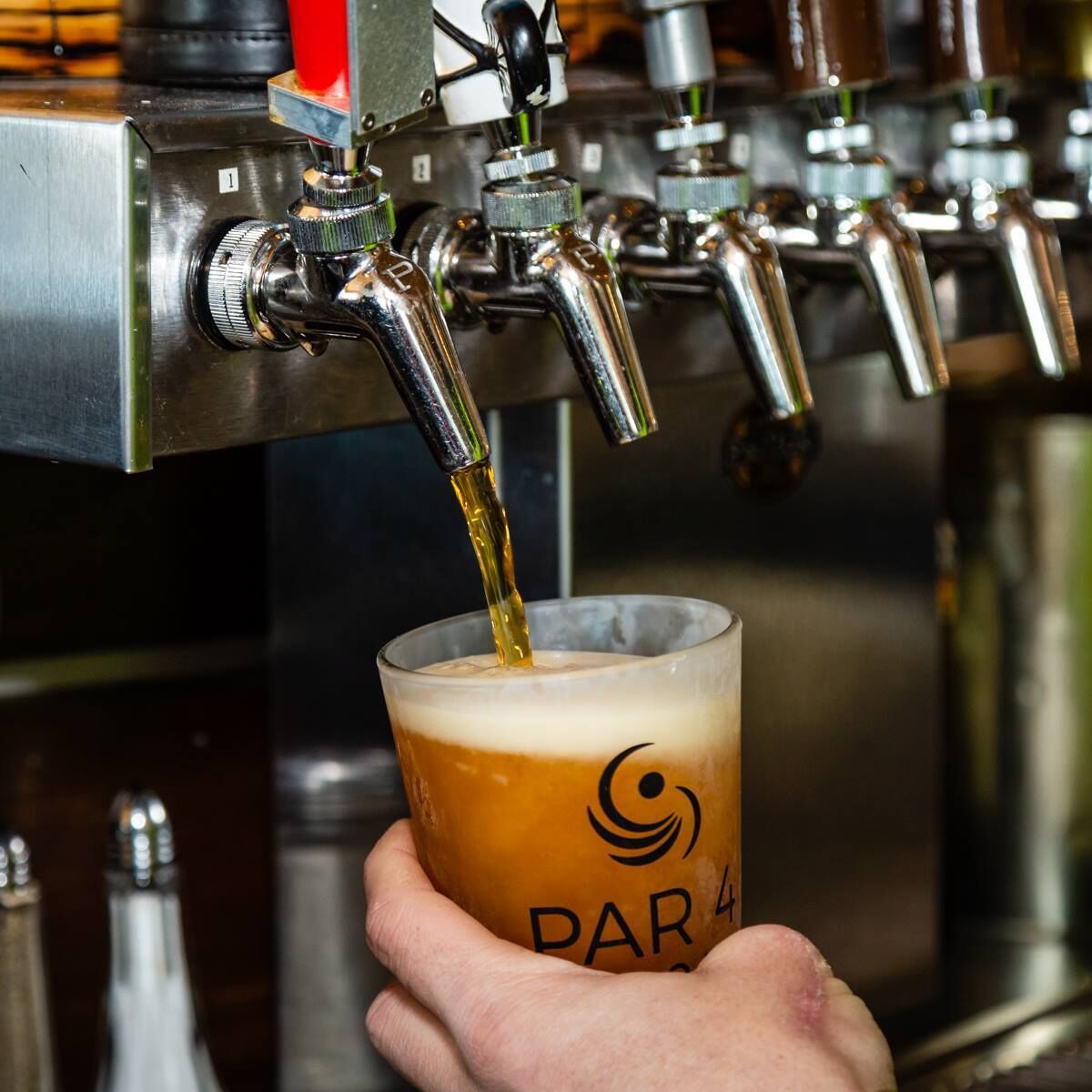 Une main tenant un verre orné d’un logo, de la bière étant versée à partir d’une tireuse.