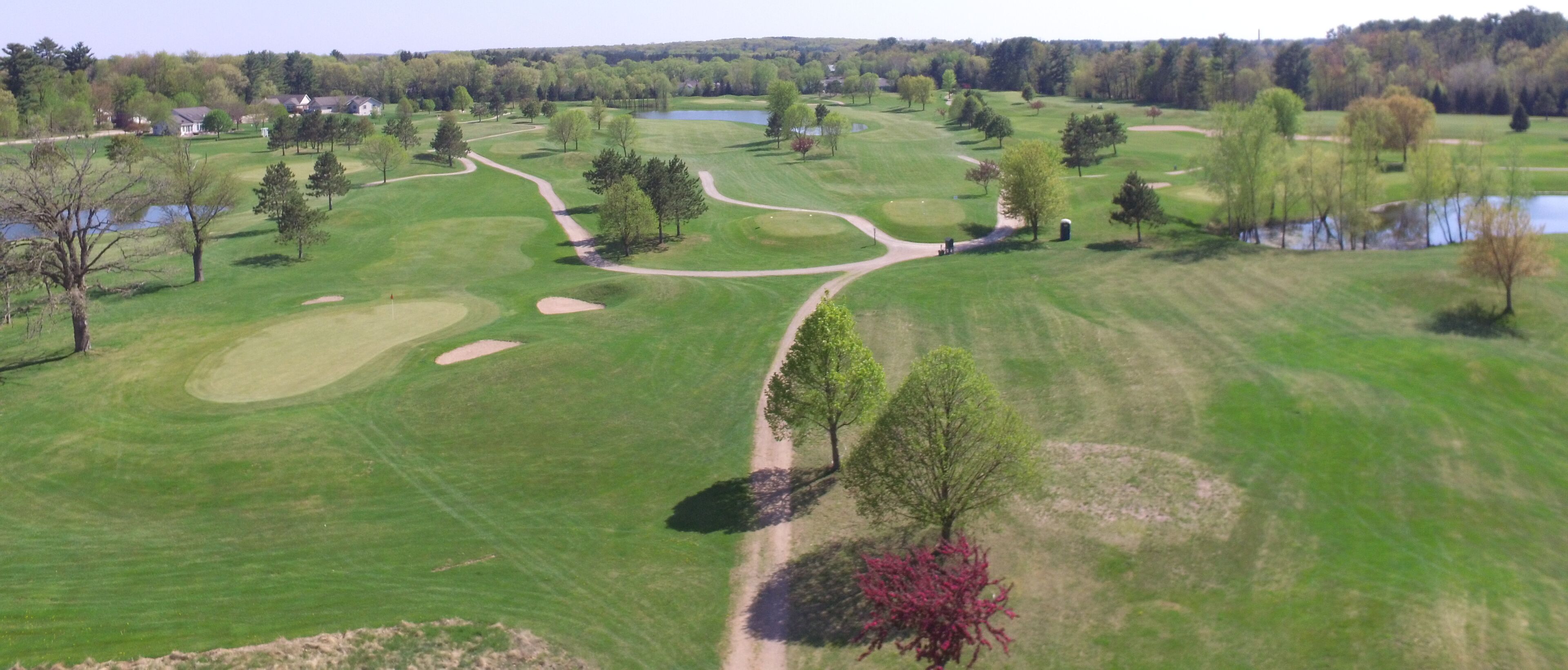 Um campo de golfe com um corpo d'água, árvores e alguns edifícios ao fundo.