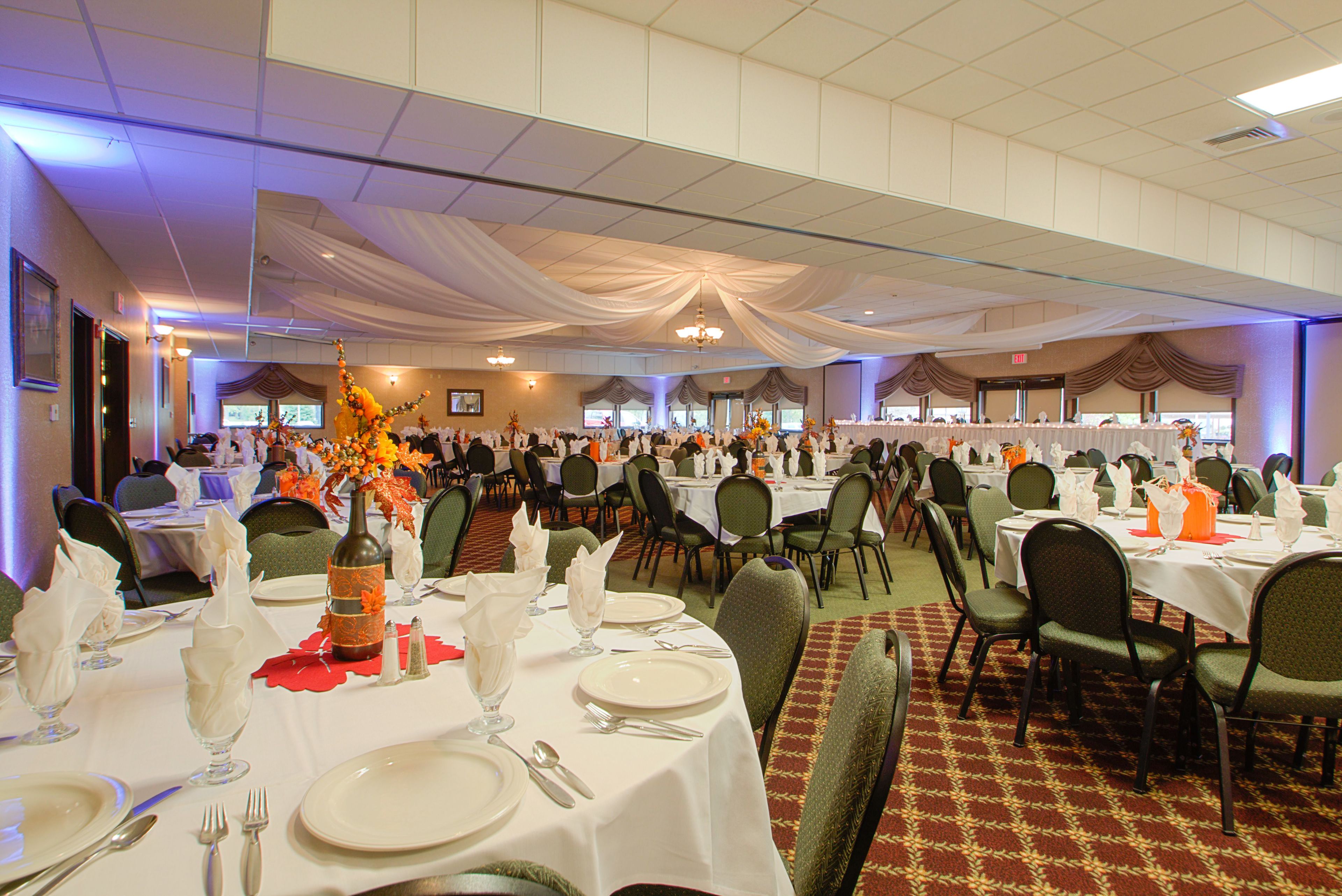 A banquet hall with round tables set for a formal event, featuring white tablecloths, silverware, and floral centerpieces.