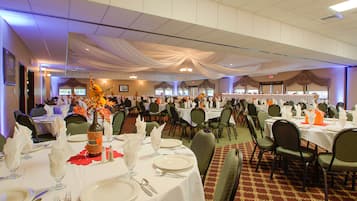 A banquet hall with round tables set for a formal event, featuring white tablecloths, silverware, and floral centerpieces.