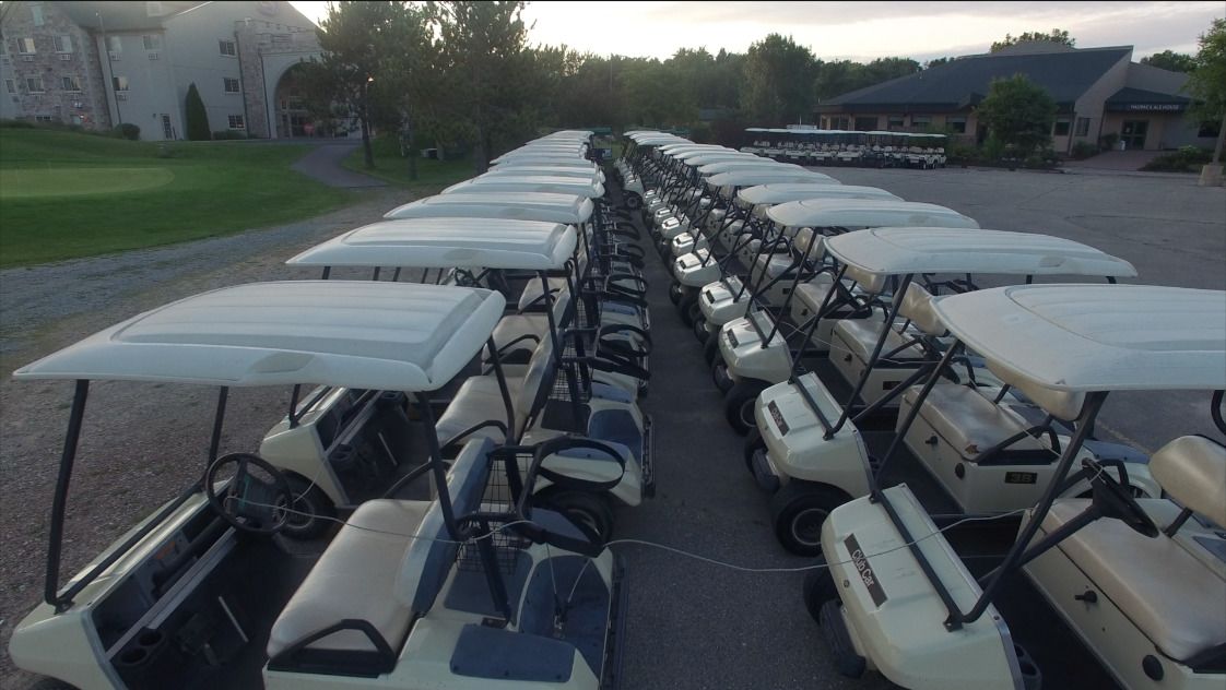 Een rij golfkarren geparkeerd op een parkeerplaats, met een gebouw op de achtergrond.
