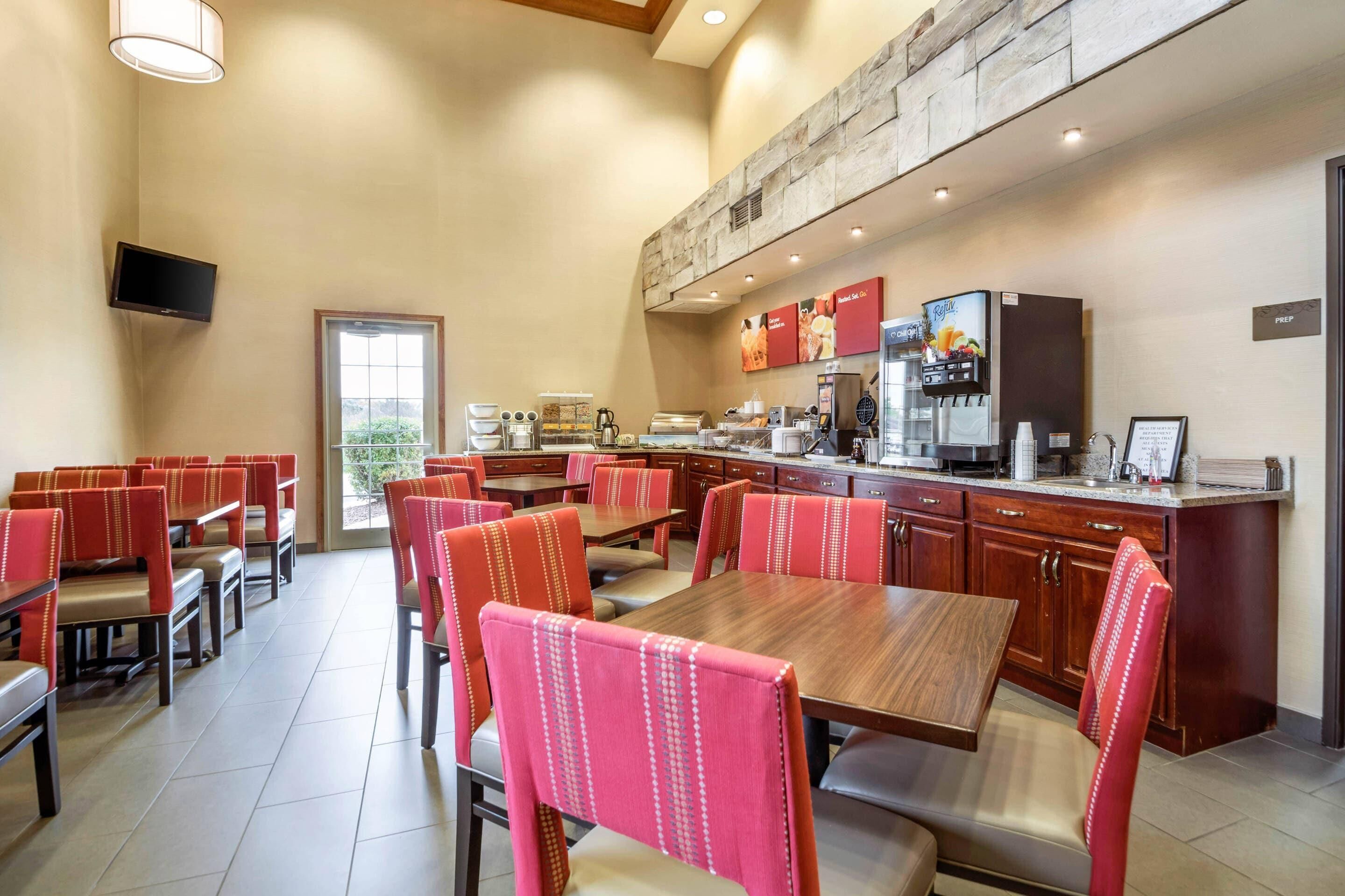 Un restaurante con cabinas y mesas, una zona de cocina y un televisor montado en la pared.