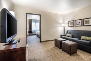 A hotel room with a flat-screen TV, a sofa, two ottomans, a lamp, and framed pictures on the wall. - Comfort Suites at Par 4 Resort (Waupaca)