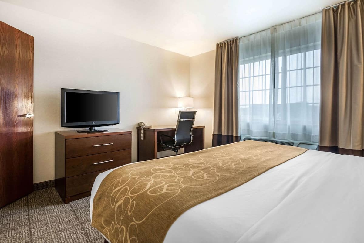 A hotel room with a bed, a desk with a chair, a television, a wardrobe, and a window with curtains.