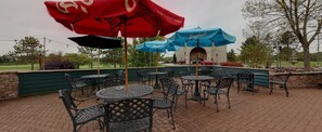 An outdoor patio with metal tables and chairs, red and blue umbrellas, and a brick wall. - Comfort Suites at Par 4 Resort (Waupaca)