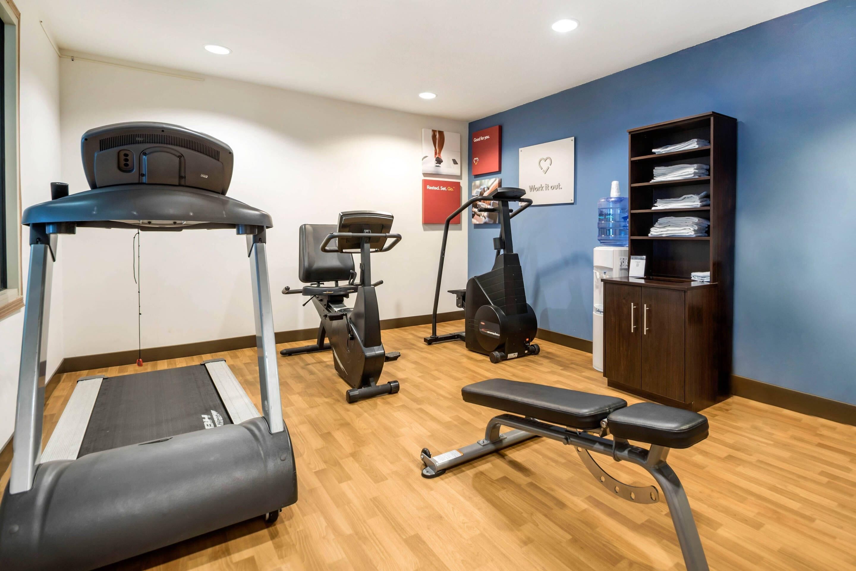 Un gimnasio con cintas de correr, bicicletas estáticas y una banca.