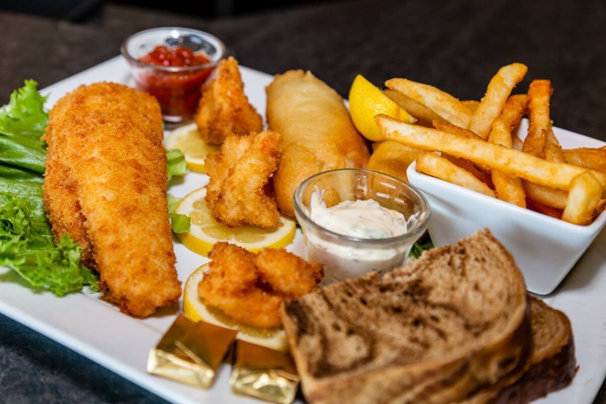 A plate of fish and chips with lemon wedges, tartar sauce, and a side of fries.