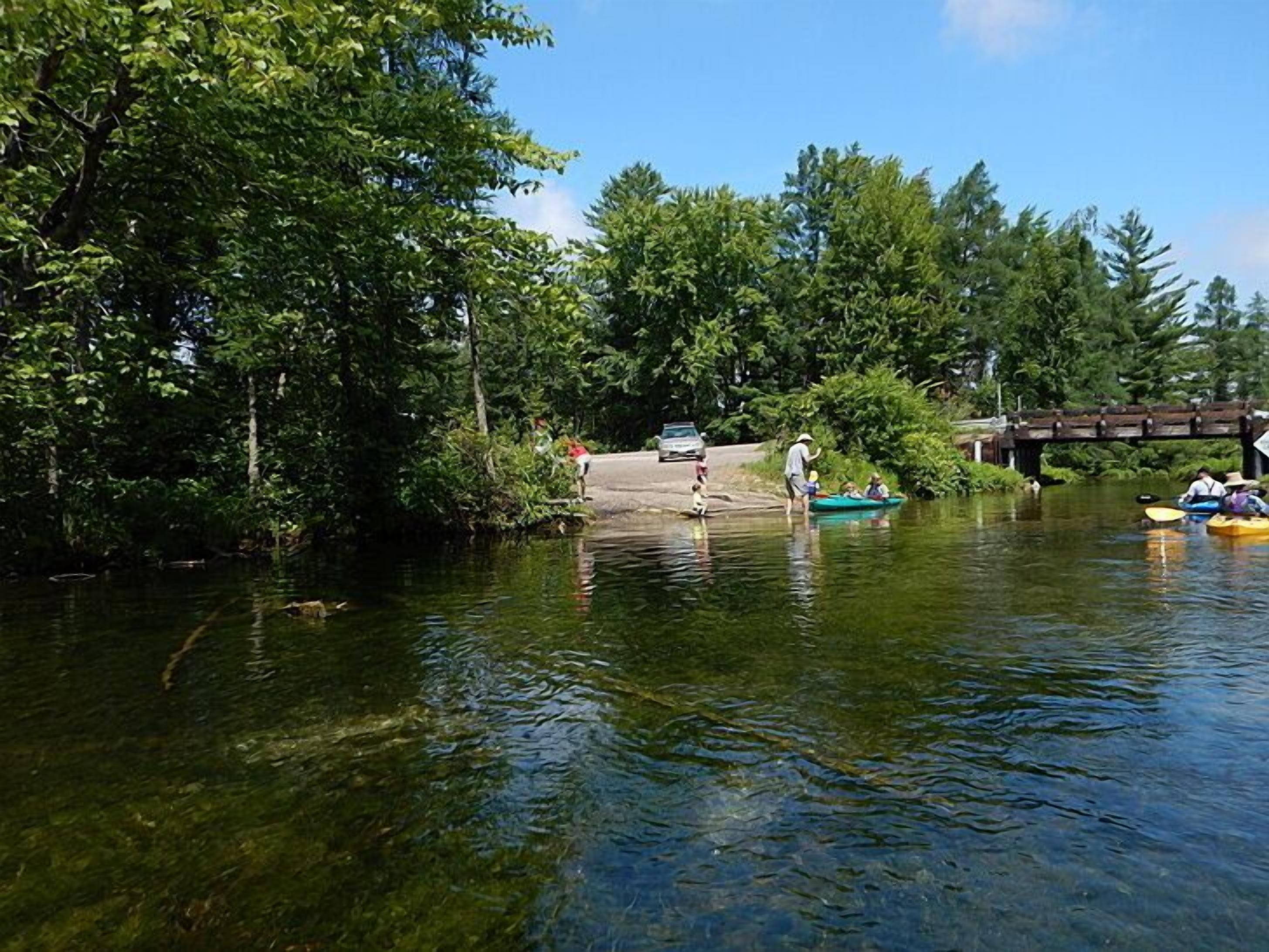 A calm river with boats, a pedestrian bridge, and dense greenery.
