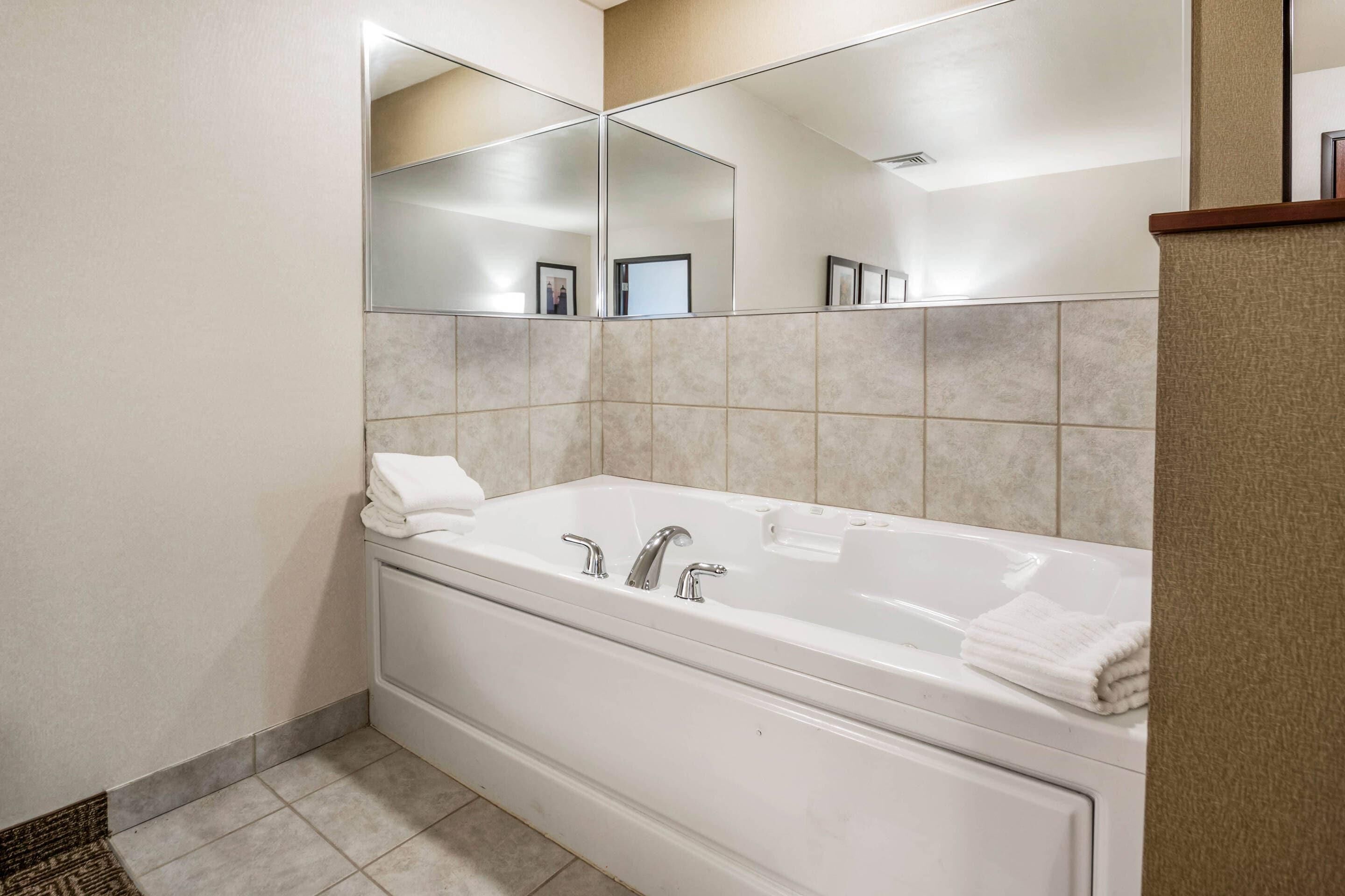 A modern bathroom with a large bathtub, a mirror, and tiled walls.