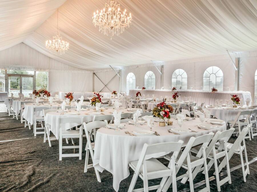 A banquet hall with round tables, white chairs, chandeliers, and large windows.