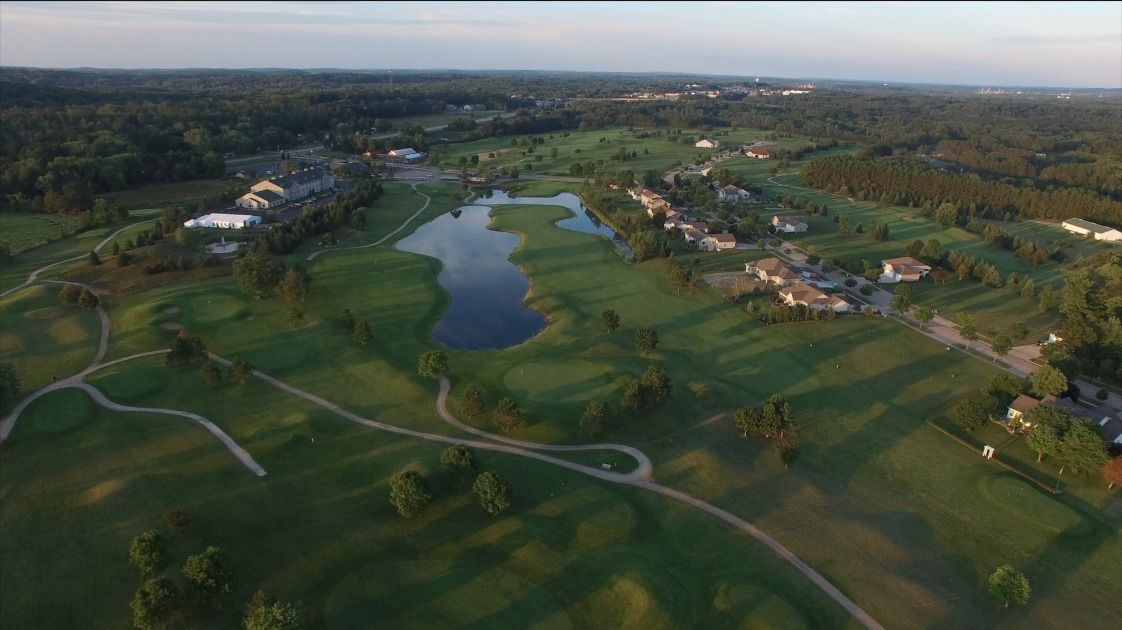 Vista aérea de un campo de golf con un estanque, casas y un edificio grande.