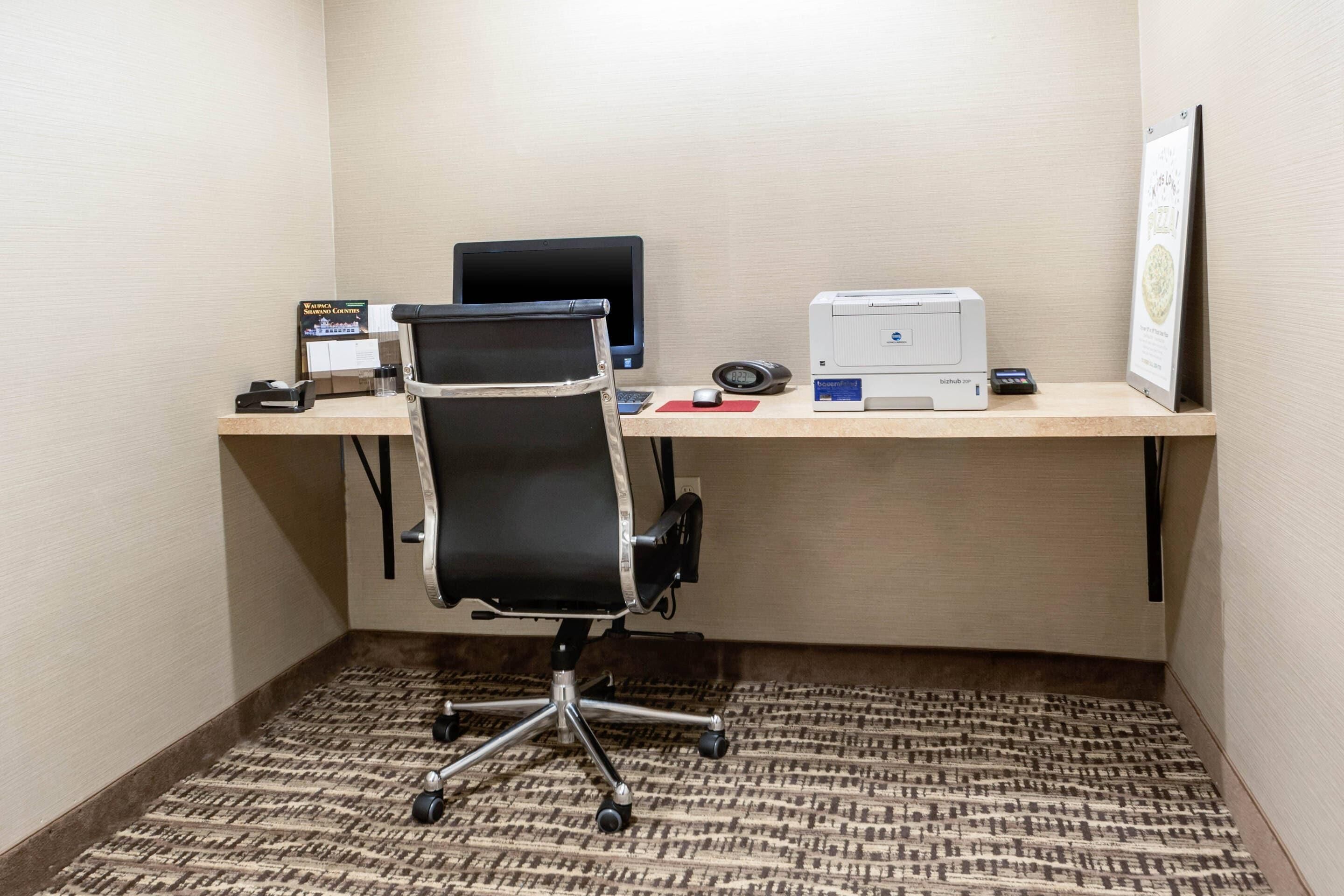 Un pequeño espacio de oficina con un escritorio, una silla, una computadora, una impresora y un certificado enmarcado en la pared.