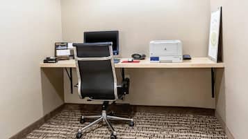 Un pequeño espacio de oficina con un escritorio, una silla, una computadora, una impresora y un certificado enmarcado en la pared.