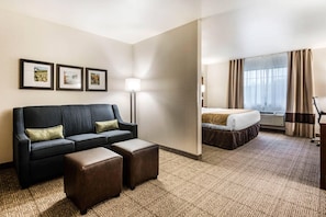 A hotel room with a sofa, two ottomans, a bed, a lamp, and three framed pictures on the wall. - Comfort Suites at Par 4 Resort (Waupaca)