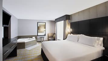 Una habitación de hotel con una cama grande, televisión, bañera, una silla y un espejo.