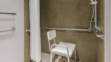 Un espace douche équipé d’une barre d’appui, d’un siège de douche blanc et d’un pommeau de douche à main.