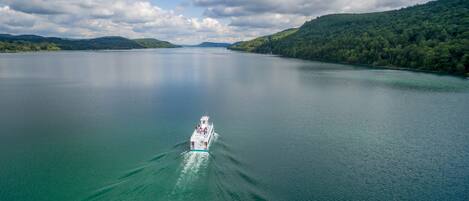Ein Boot auf einem ruhigen See mit Bergen im Hintergrund und einem teilweise bewölkten Himmel.