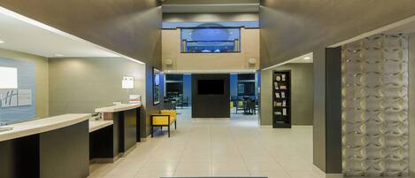 A hotel lobby with a reception desk, seating area, and a staircase leading to an upper level.