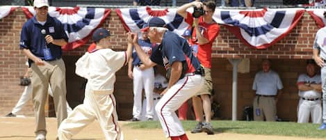 A baseball game with players in action, spectators in the background, and a brick wall with a flag.