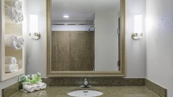 Un baño con encimera de granito, un lavabo y un espejo. Hay toallas en la pared y se ve una ducha en el espejo.