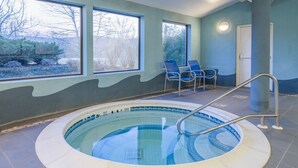 A swimming pool with a metal ladder, two blue chairs, and a door in a room with blue walls and windows. - Holiday Inn Express & Suites Cooperstown by IHG (Cooperstown)