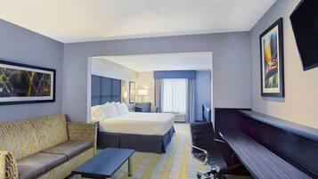 A hotel room with a bed, a desk, a chair, a sofa, and a flat-screen TV.
