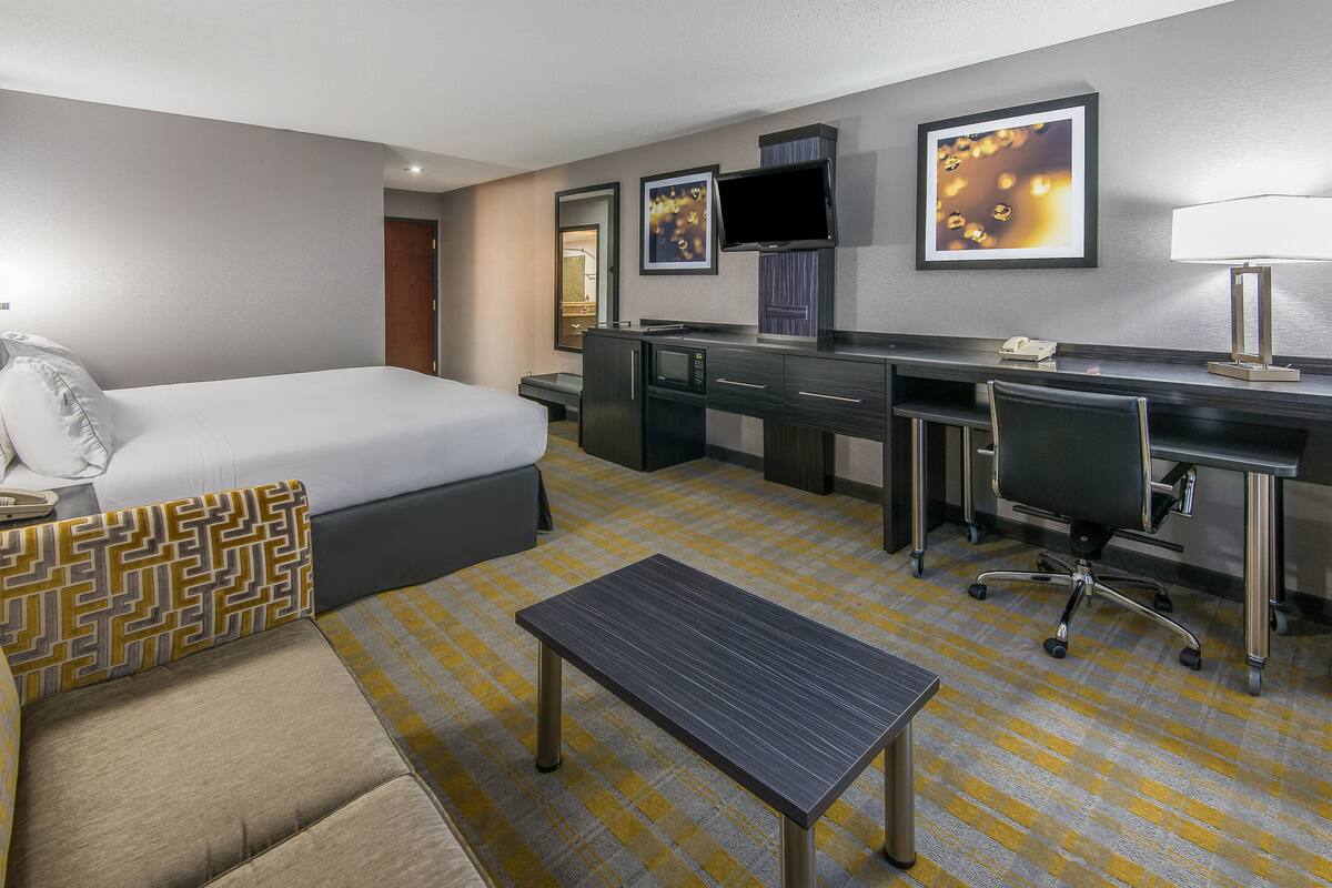 Ein Hotelzimmer mit Bett, Schreibtisch, Stuhl, kleinem Tisch und Fernseher an der Wand.