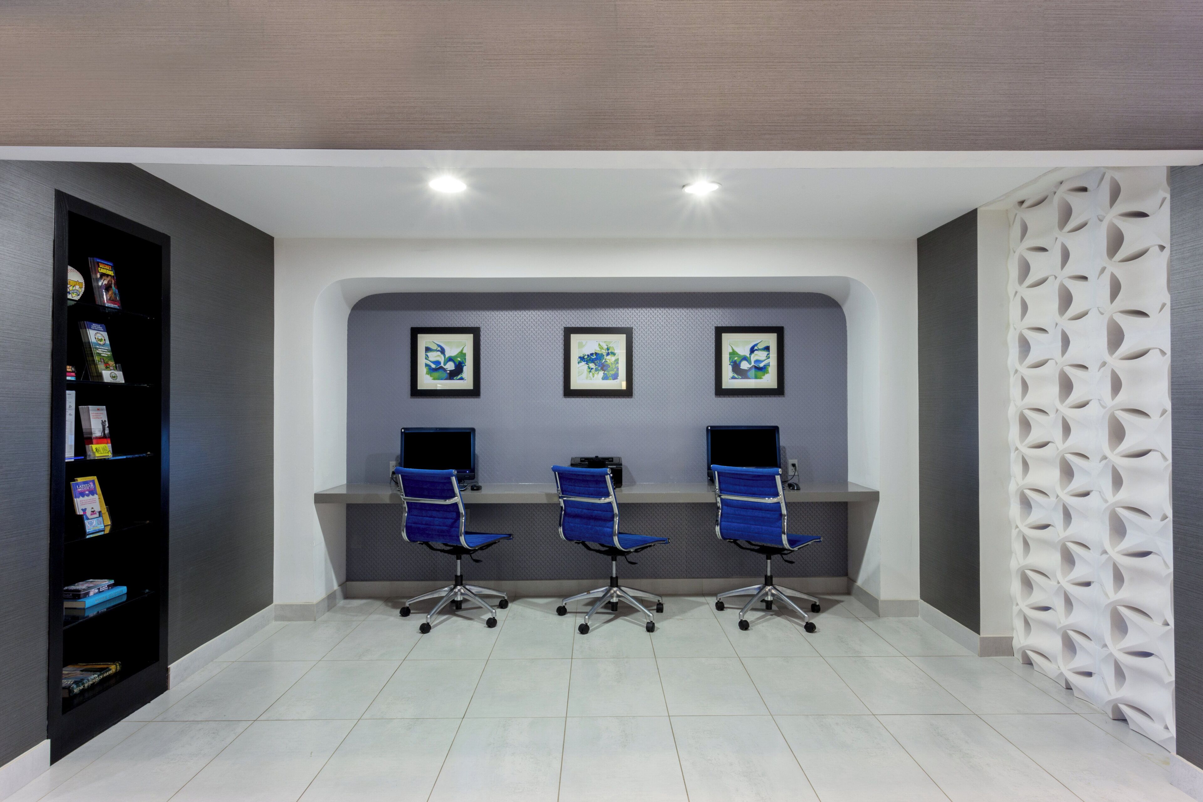 A reception area with three blue office chairs, a wall-mounted computer station, and a decorative white wall panel.