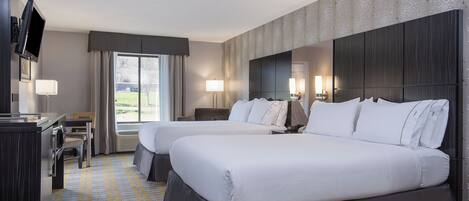 A hotel room with two beds, a desk, a TV, and a view of the outdoors.