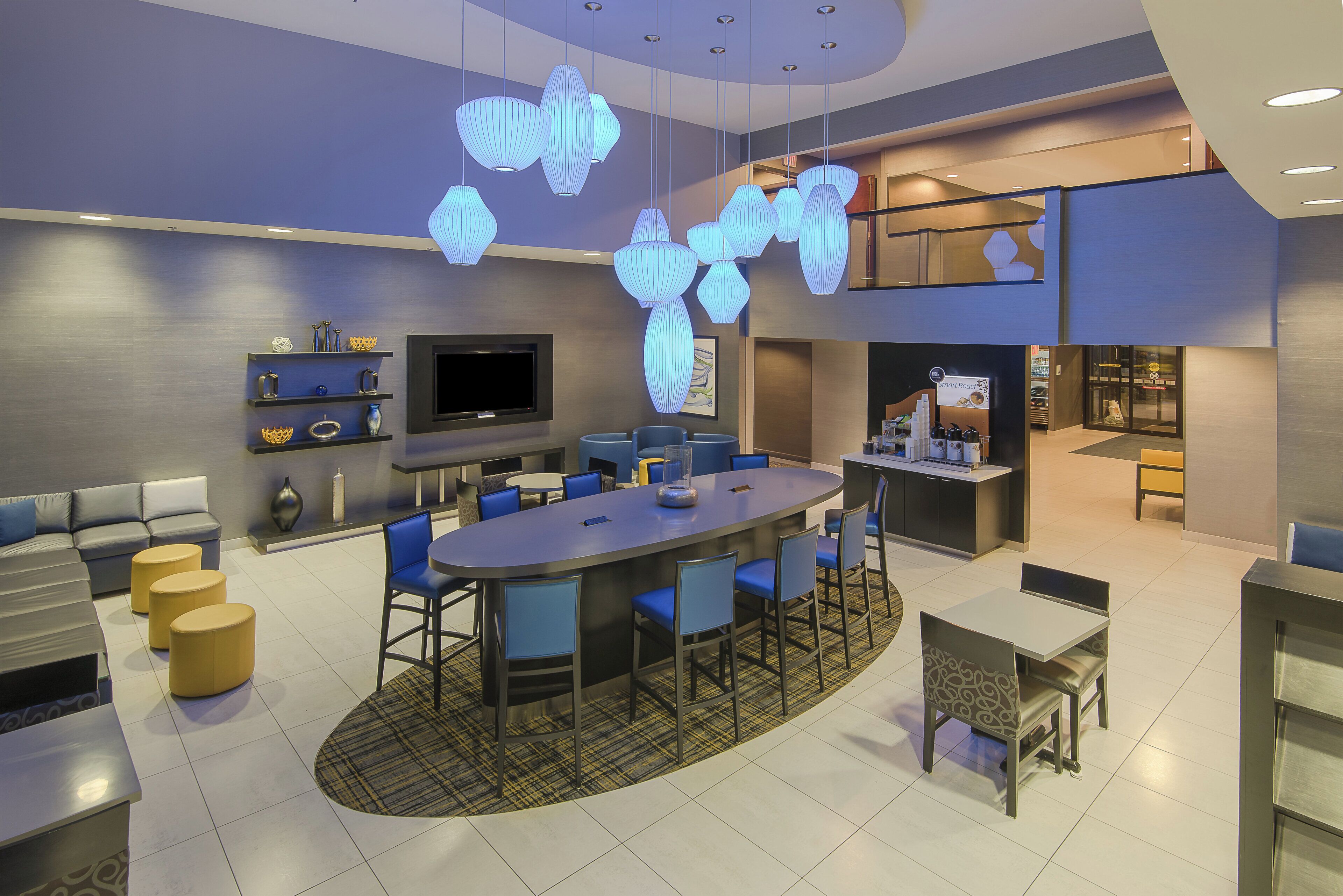 A modern dining area with a central round table, blue chairs, and a flat-screen TV mounted on the wall.
