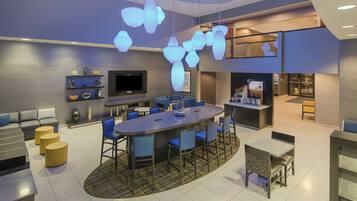 A modern dining area with a central round table, blue chairs, and a flat-screen TV mounted on the wall.
