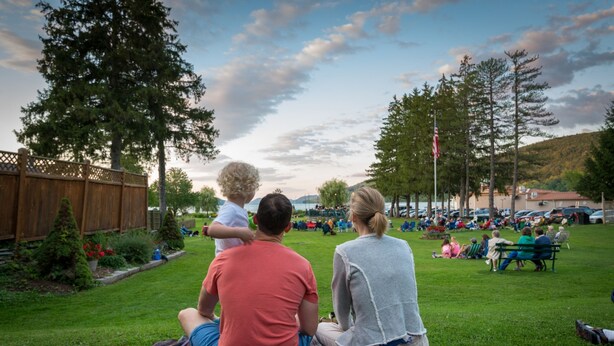 Une famille est assise sur une couverture dans un espace verdoyant, avec des arbres et une clôture en arrière-plan.