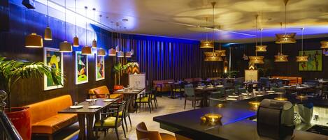 A modern restaurant with multiple dining areas, including a bar and seating with tables and chairs.