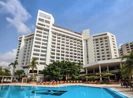 Un hotel moderno con un amplio área de piscina, varios pisos y una fachada blanca destacada.