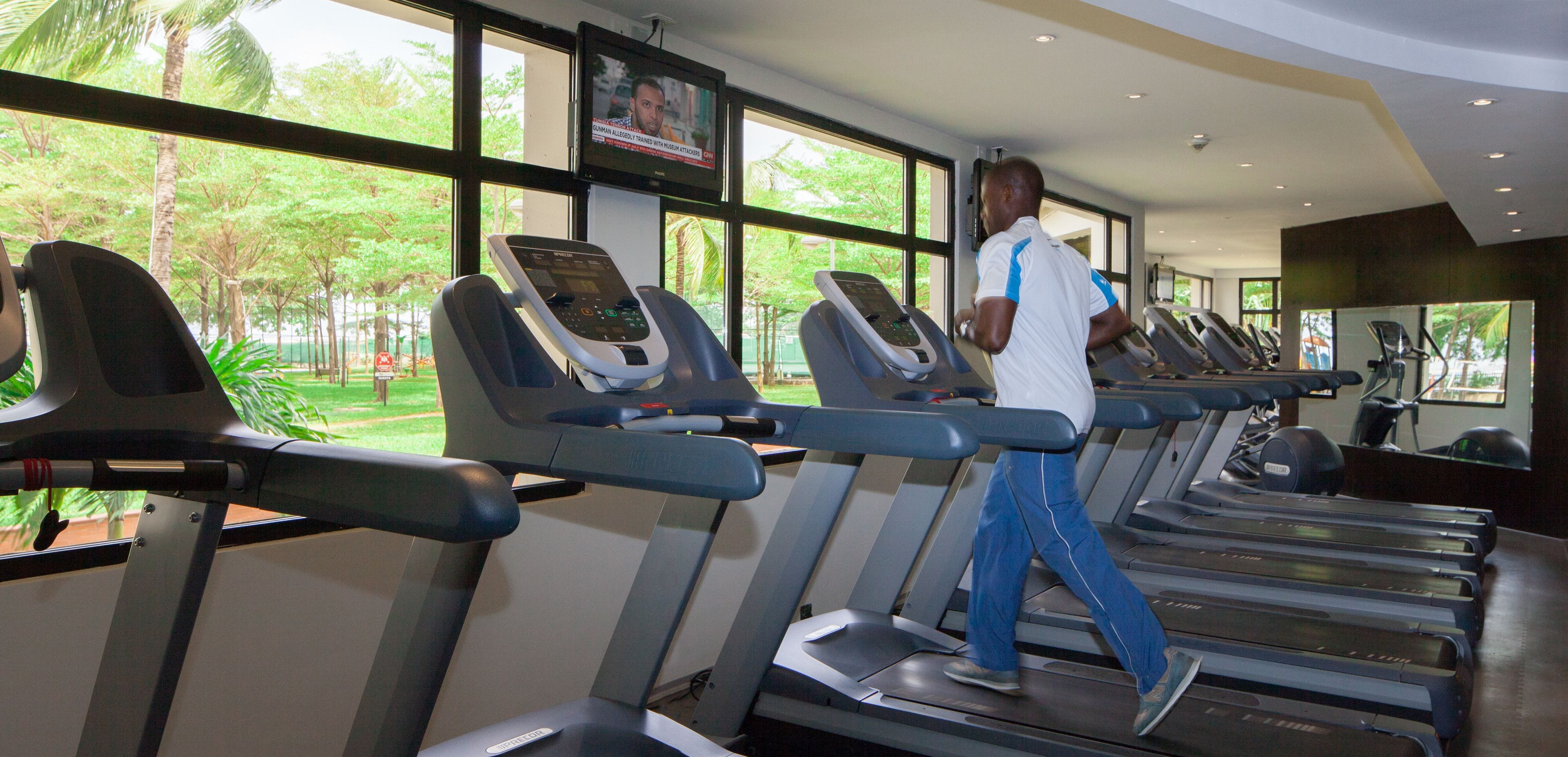 A gym with treadmills, a TV screen, and large windows with a view of greenery.