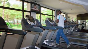 A gym with treadmills, a TV screen, and large windows with a view of greenery.